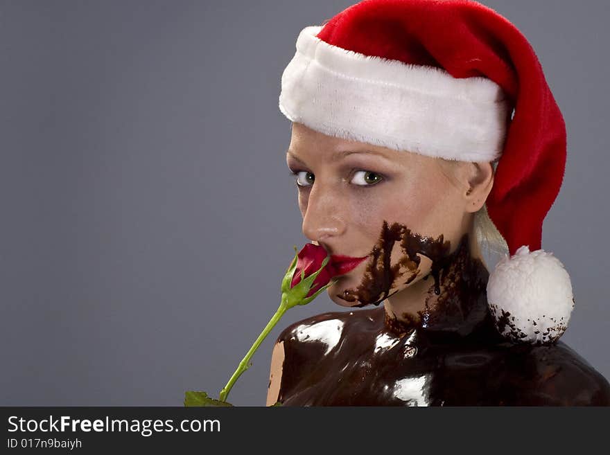 Attractive naked blond girl covered in chocolate wearing a santa hat and holding red rose. Attractive naked blond girl covered in chocolate wearing a santa hat and holding red rose