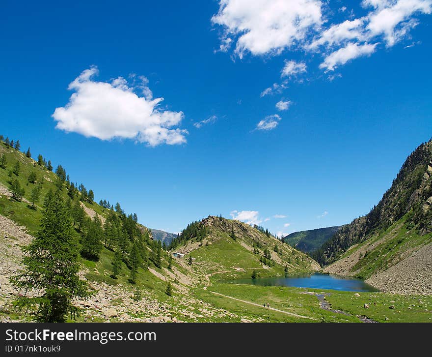 A mountain landscape with a blue lake surronded by green vegetation, with a nice blue sky full of white clouds. A mountain landscape with a blue lake surronded by green vegetation, with a nice blue sky full of white clouds.