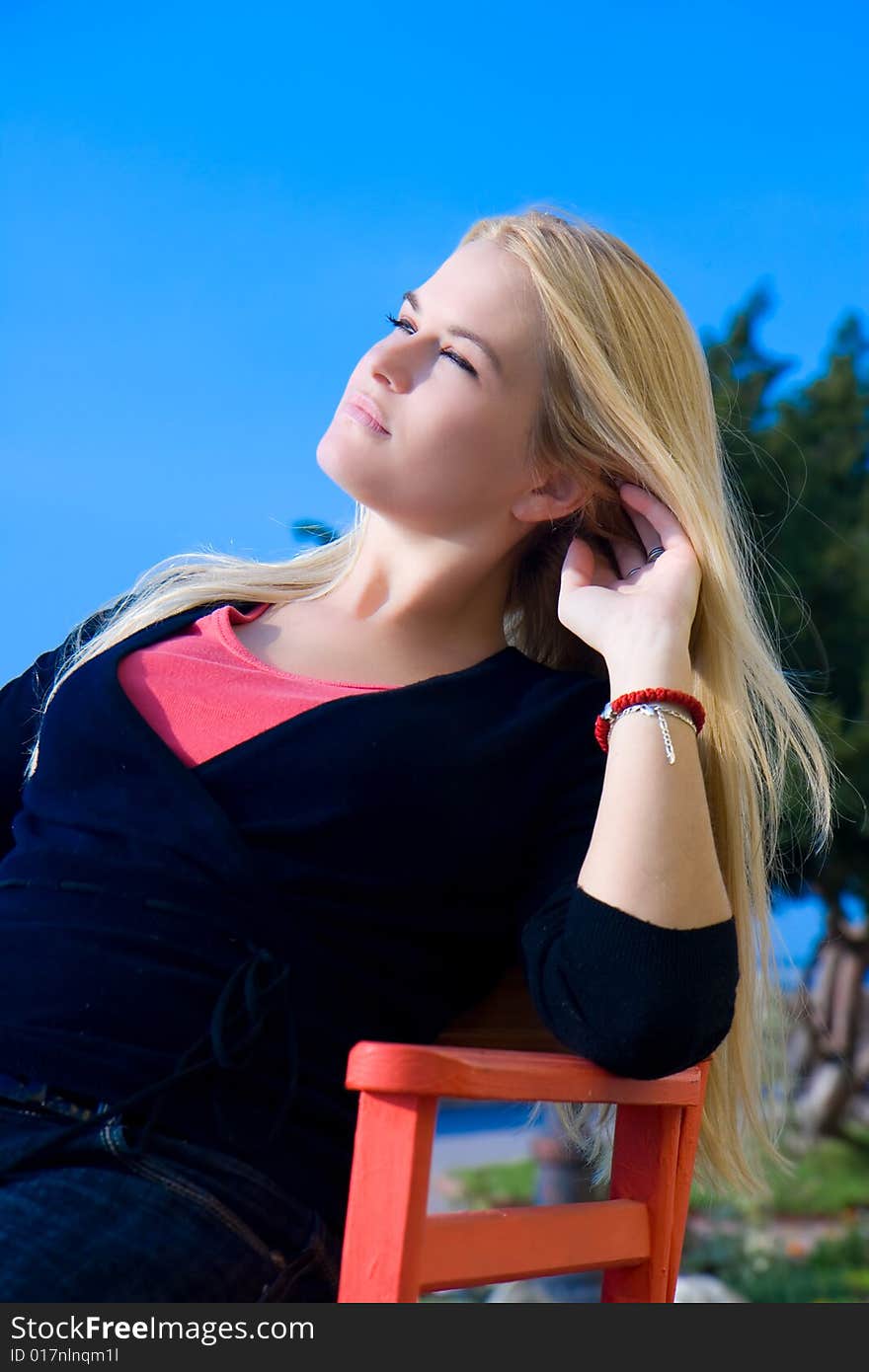 Beautiful blondy sitting on red chair  in sun