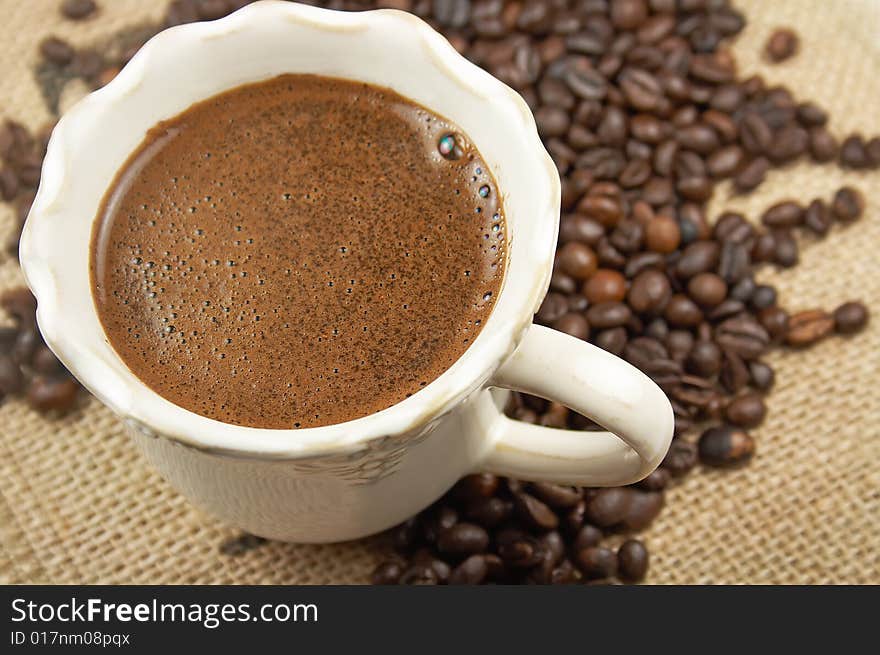 Cup of aromatic coffee and coffee beans on webbing material. Cup of aromatic coffee and coffee beans on webbing material