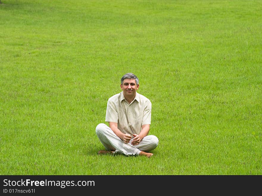 Smiling man sitting on grass field. Smiling man sitting on grass field