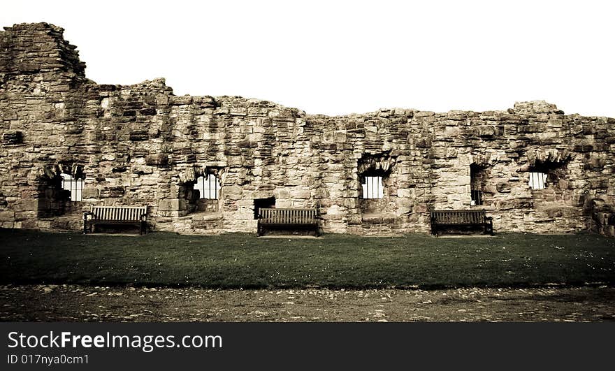 Three benches in front of a ruined stone castle wall