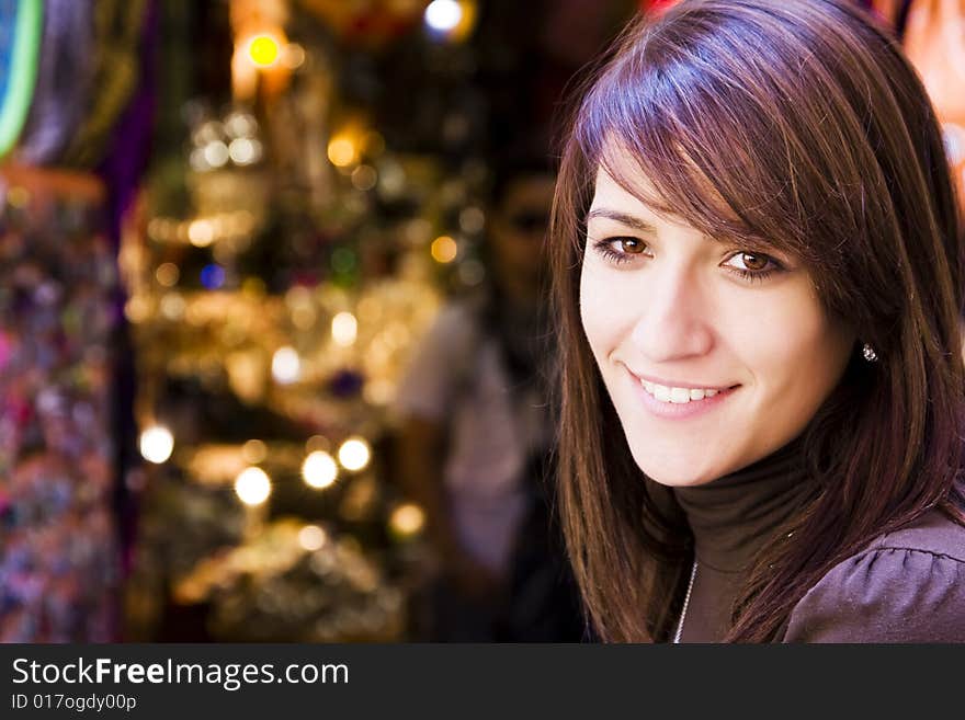 Smiling young woman with small shop as background.