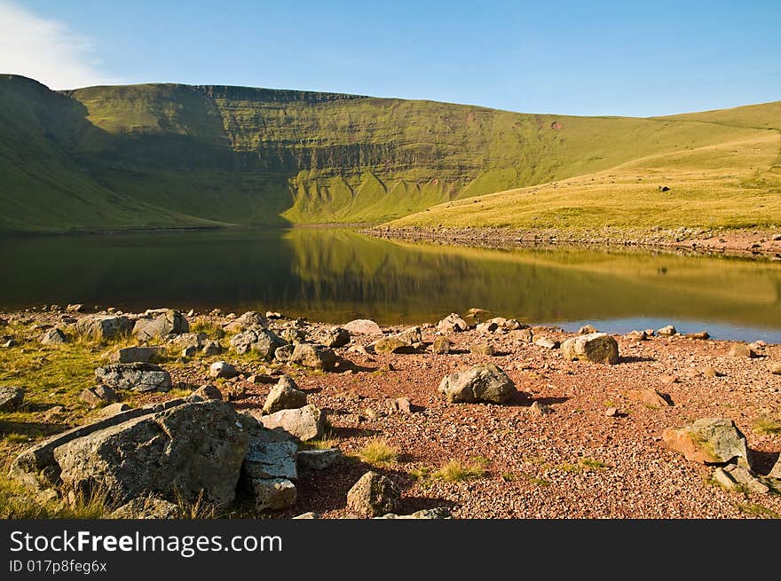 A calm welsh lakes reflects the background peaks in it's still waters.