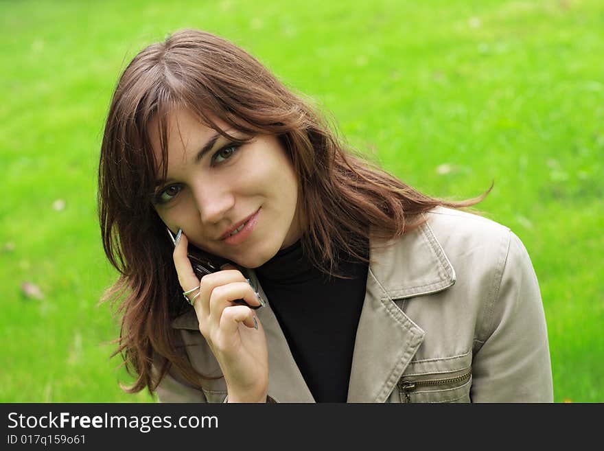 Beautiful young girl with a phone, over green grass background