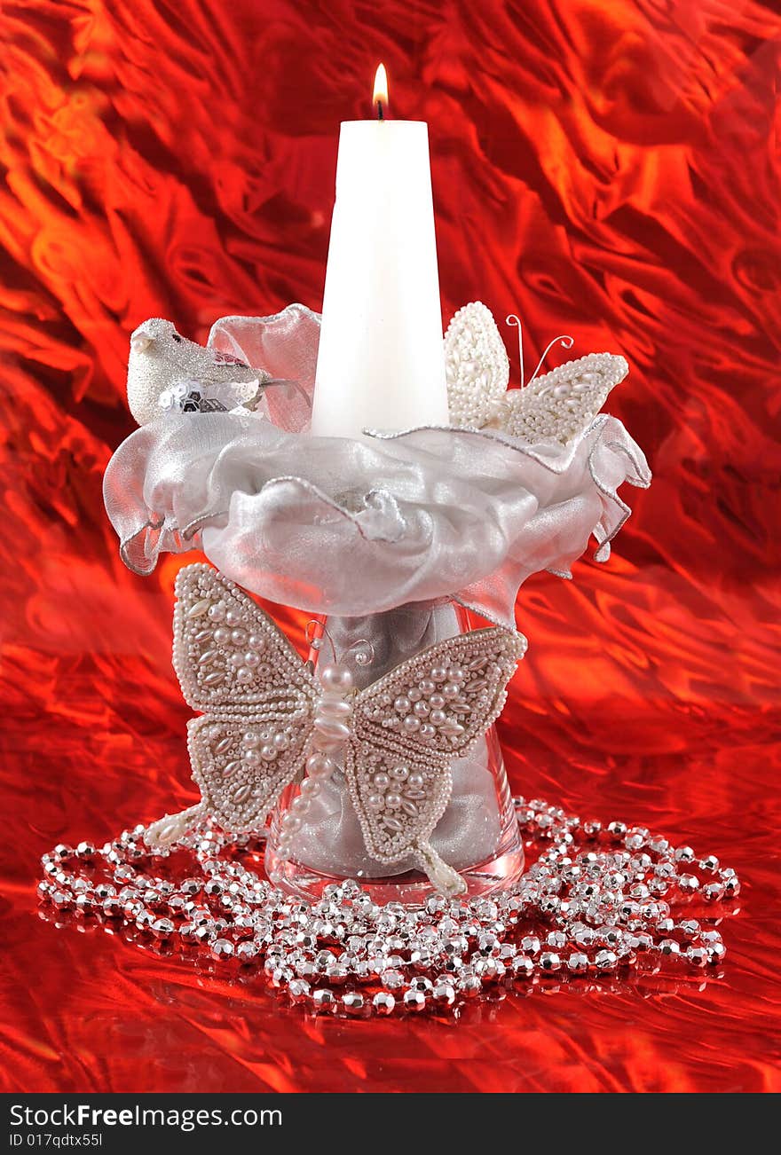 Tall christmas composition with silver baterflies, bird, ribbons, beads and lit candle on shiny red background. Tall christmas composition with silver baterflies, bird, ribbons, beads and lit candle on shiny red background