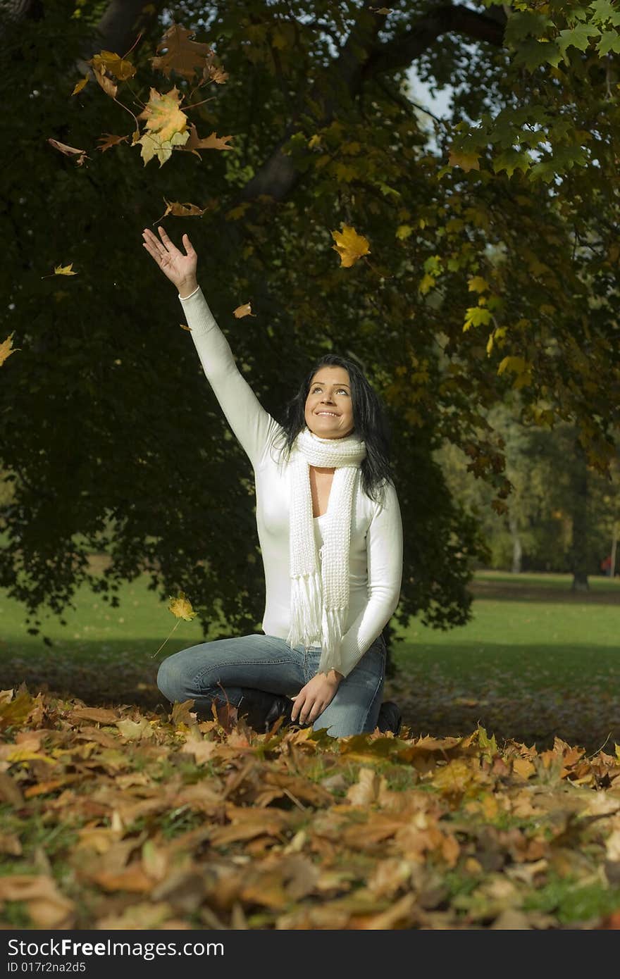 Girl having a lot of fun with falling leaves in autumn