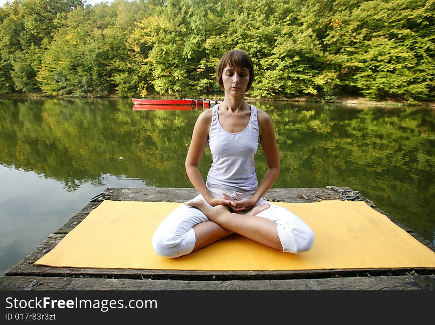 Woman doing yoga on lake in park in autumn