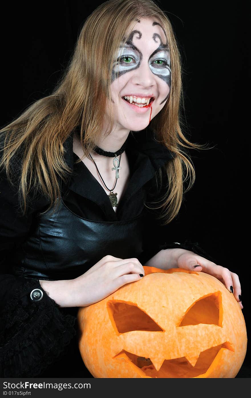 Laughing vampire girl with halloween pumpkin, on black background