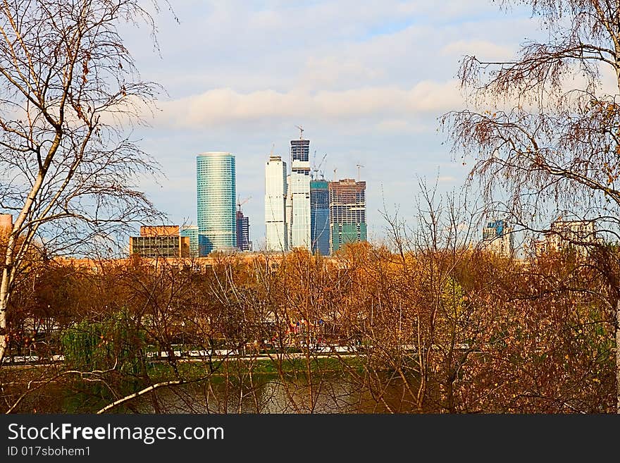 Building of high-rise buildings, in the foreground trees grow, sky in clouds. Building of high-rise buildings, in the foreground trees grow, sky in clouds