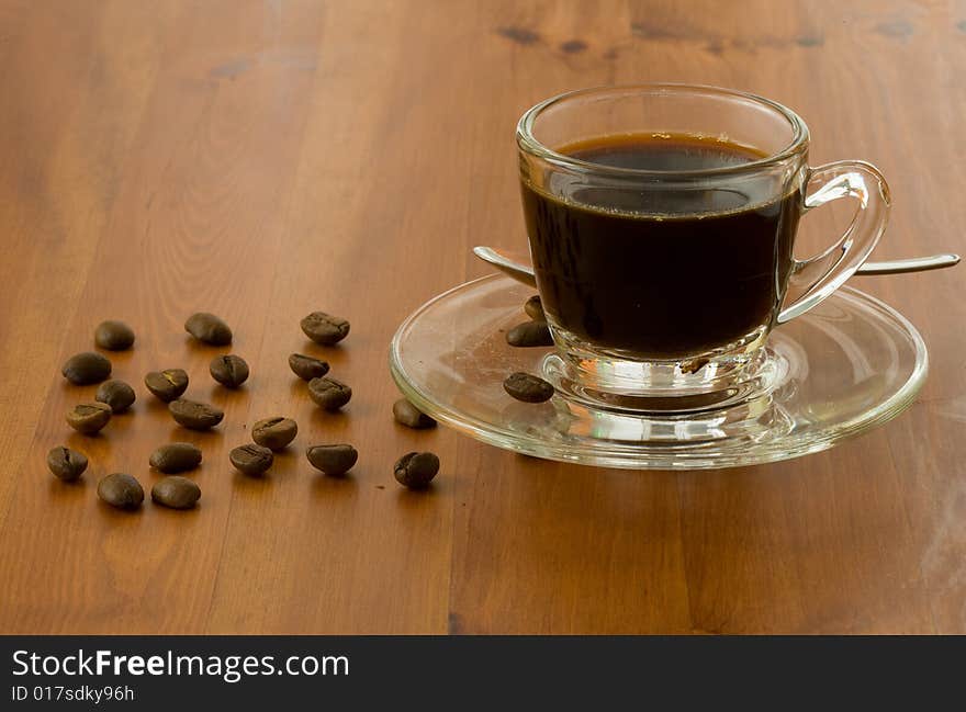 A cup of dark coffee with beans over wood background