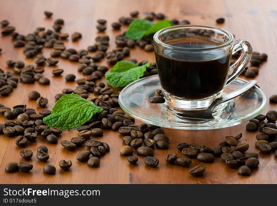 A cup of dark coffee with beans over wood background