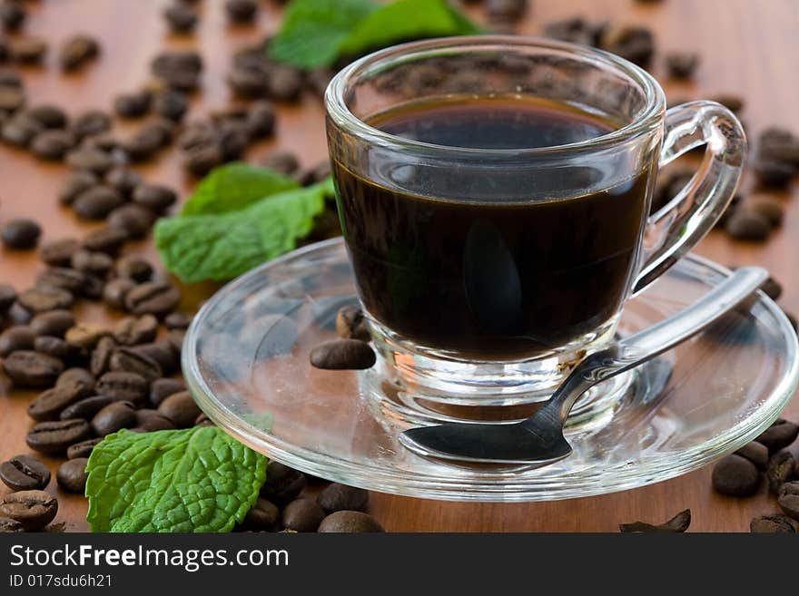 A cup of dark coffee with beans over wood background