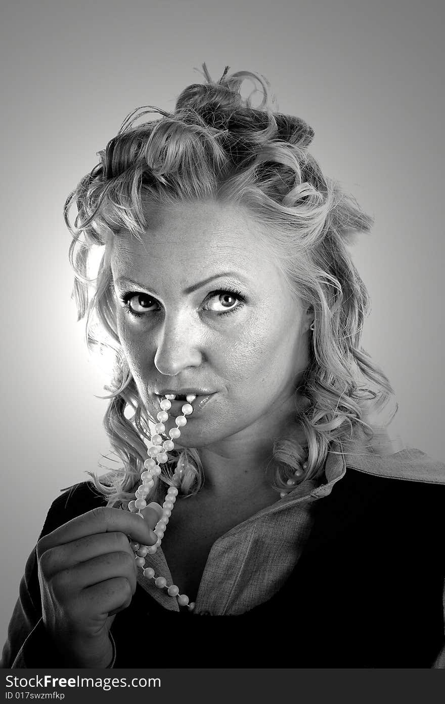 A woman with curly blonde hair with pearls in her mouth lit with spot in black and white. A woman with curly blonde hair with pearls in her mouth lit with spot in black and white