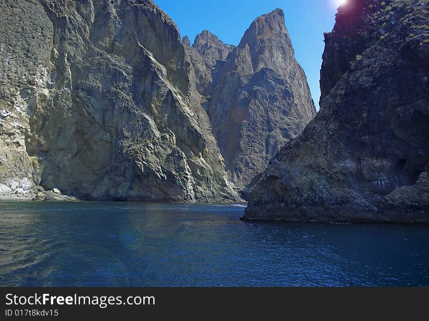 Rocky volcanic mountains among sea and against blue sunny sky. Rocky volcanic mountains among sea and against blue sunny sky