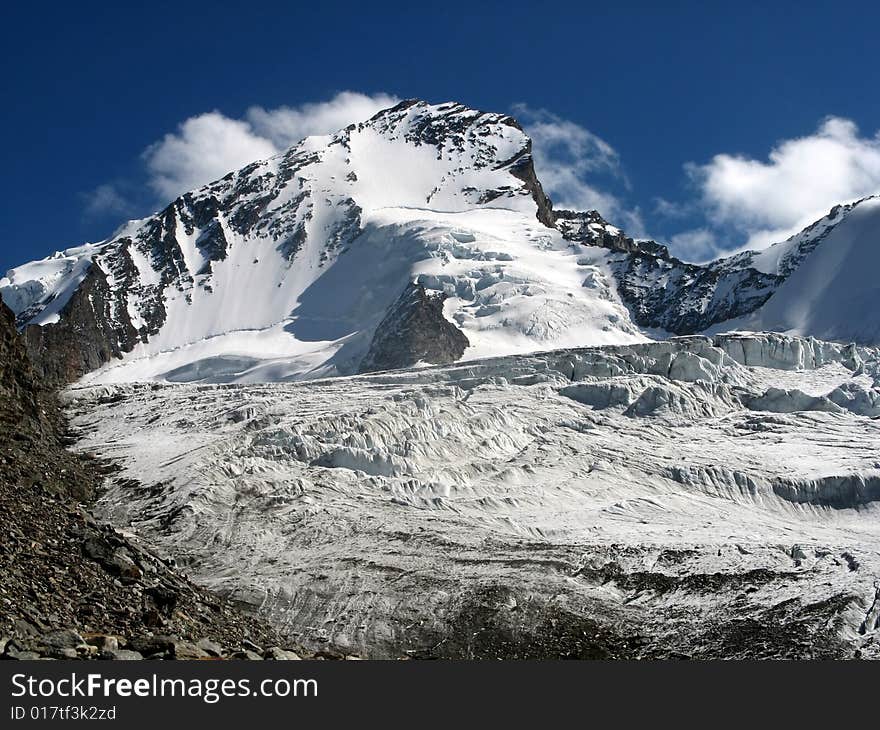 South face of Dom - highest mountain within Switzerland, covered with snow, under blue sky and white clouds, above glacier. South face of Dom - highest mountain within Switzerland, covered with snow, under blue sky and white clouds, above glacier