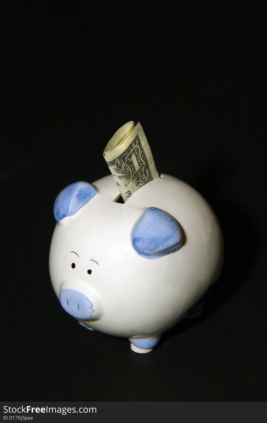 On a black, nutral background sits a piggybank with a dollar sticking out of it. On a black, nutral background sits a piggybank with a dollar sticking out of it.