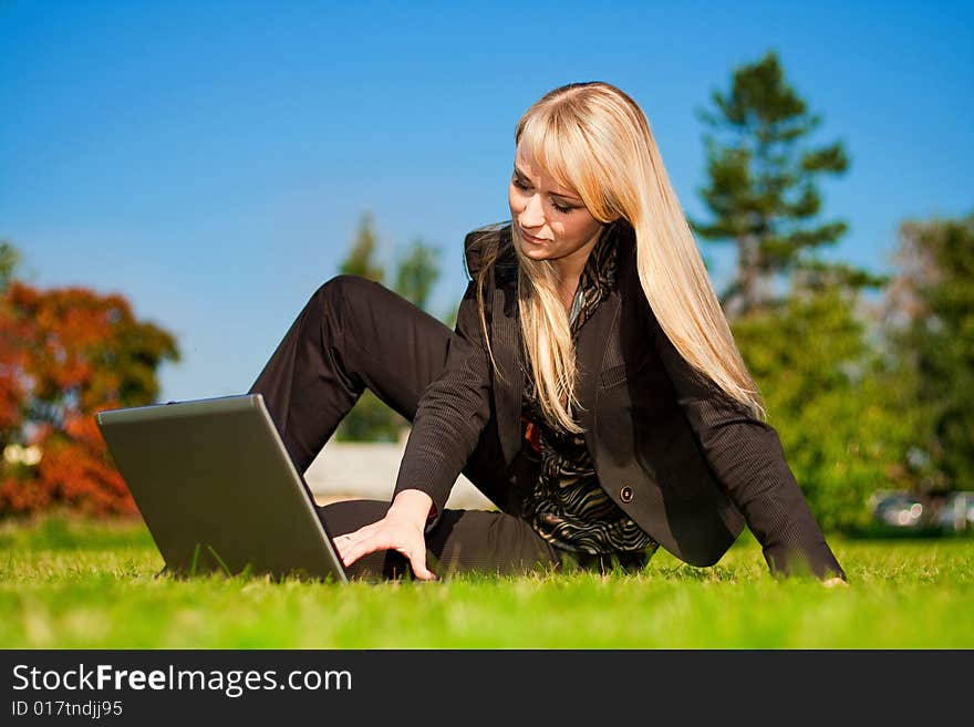 Young blonde businesswoman working on laptop computer in a meadow