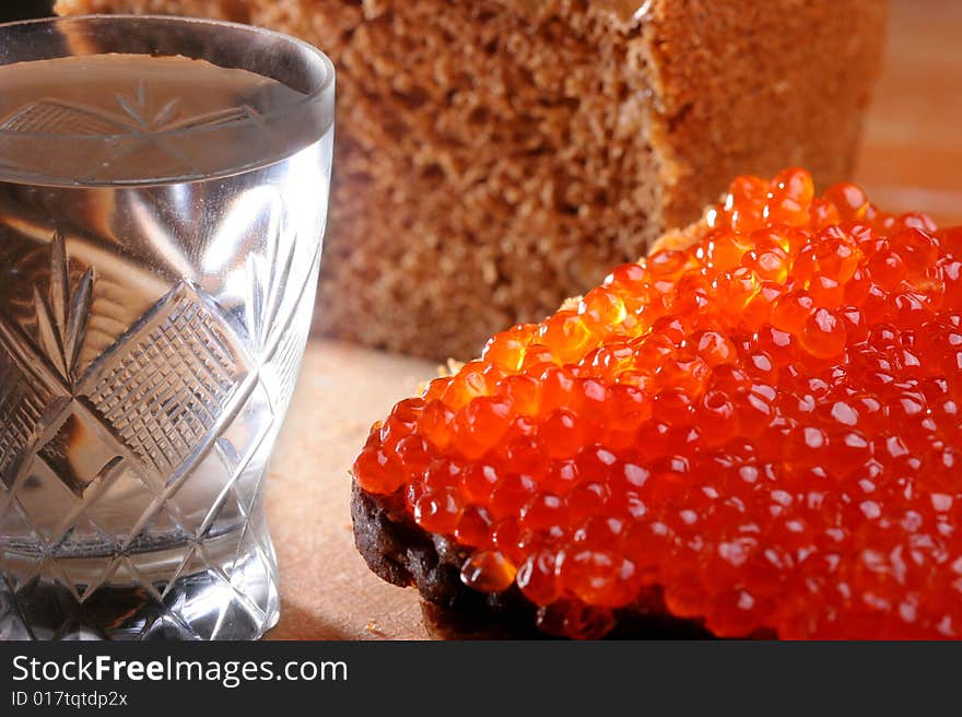 Red caviar, brown bread on a wooden board. Vodka is in a wineglass.