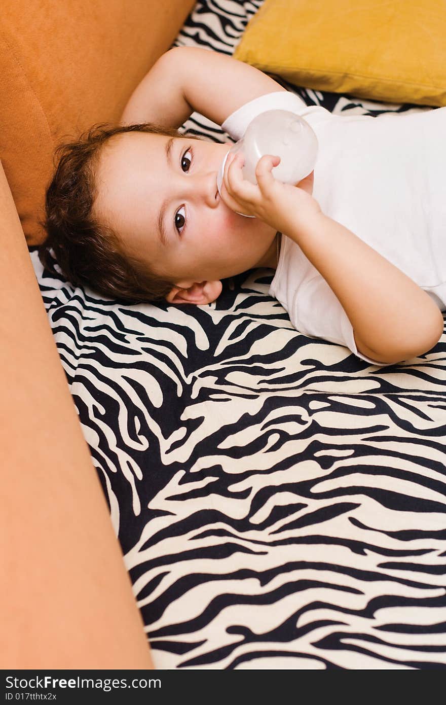 Small boy drinking milk from a bottle lying on a sofa