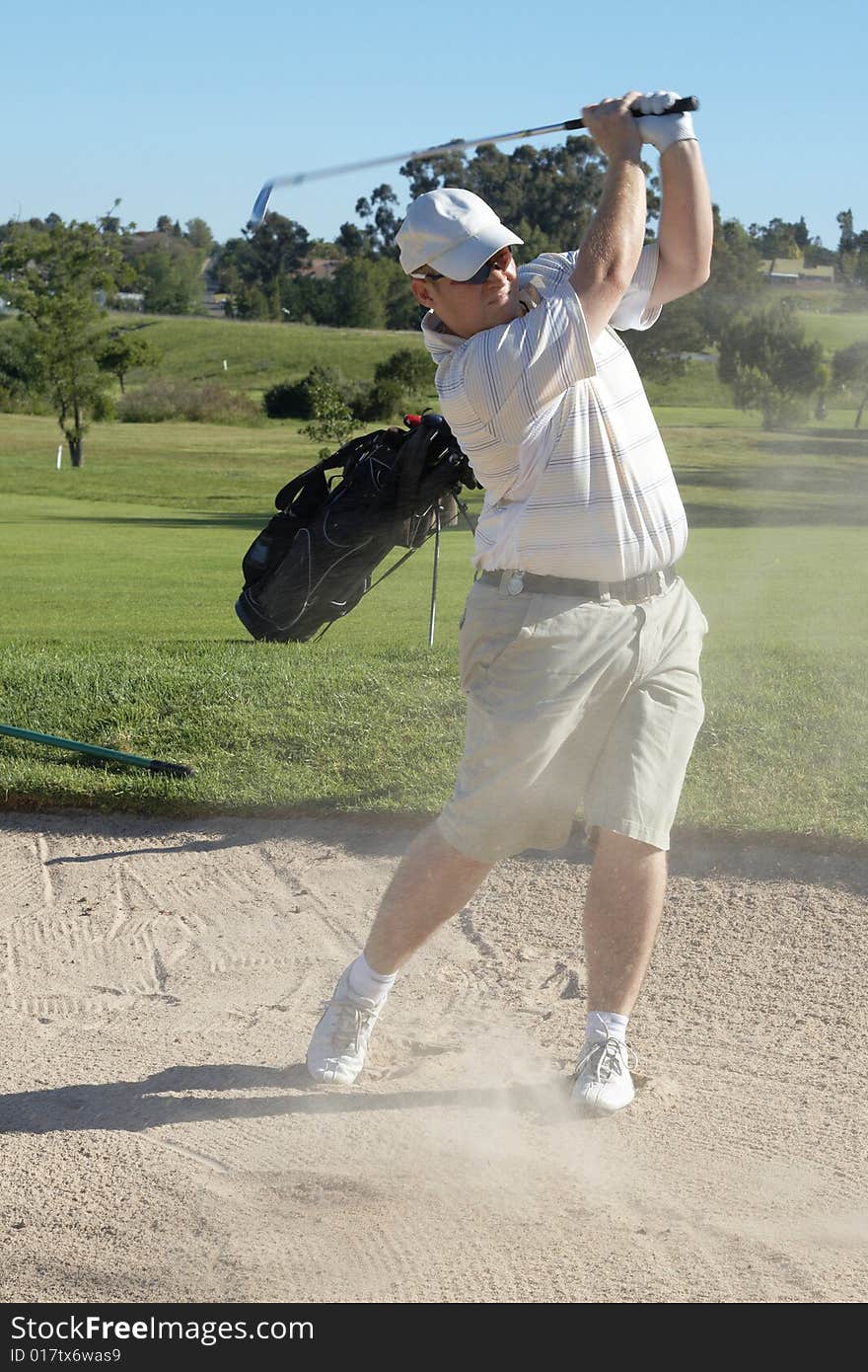 Golfer hitting the ball out of the sand bunker with sand being sprayed all over. Nice summer day. Golfer hitting the ball out of the sand bunker with sand being sprayed all over. Nice summer day