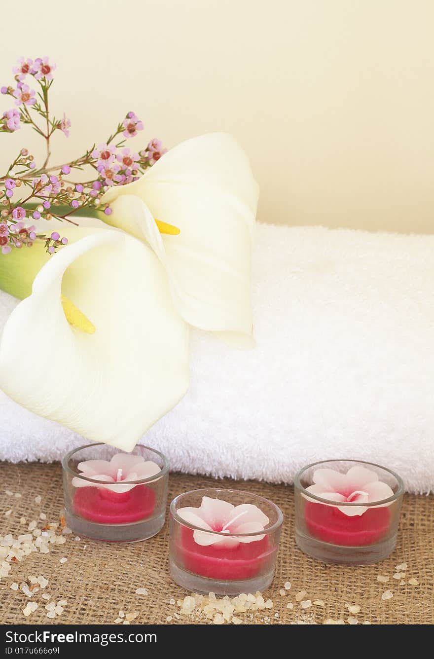 Relaxing spa scene with a white rolled up towel, white lillies, beautiful handmade candles and bath salts