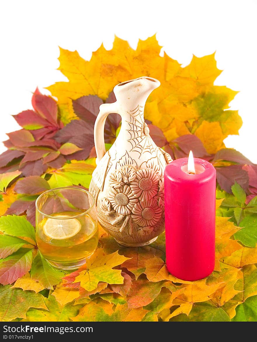 Decorative ceramic jug with wine glass of cognac and lemon red burning candle on carpet from maple autumn leaves