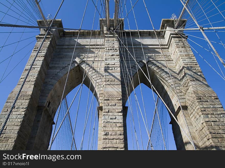 Brooklyn Bridge's arches and cables against the blue sky.