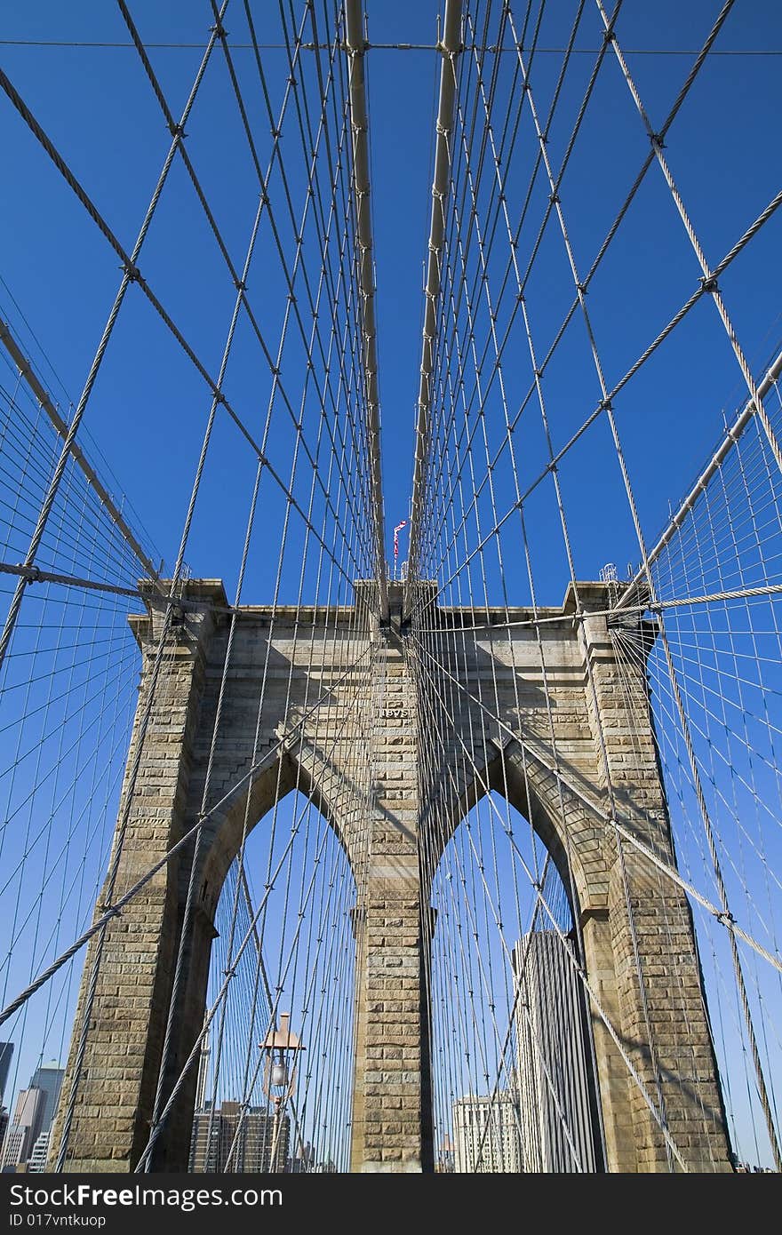 Brooklyn Bridge's arches and cables against the blue sky.