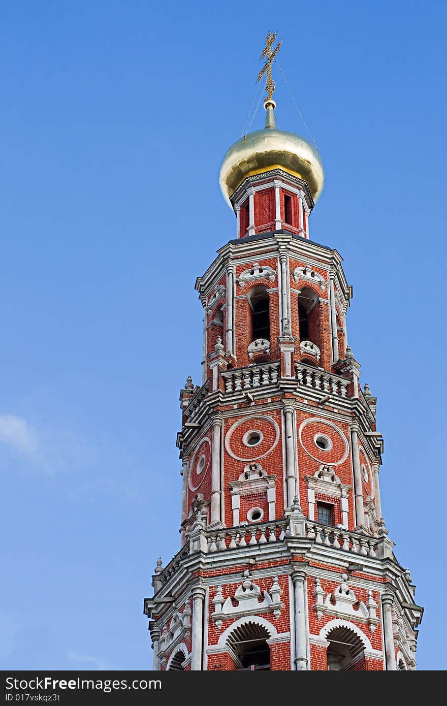 Against the blue sky a high belltower from a red brick, with a gold dome