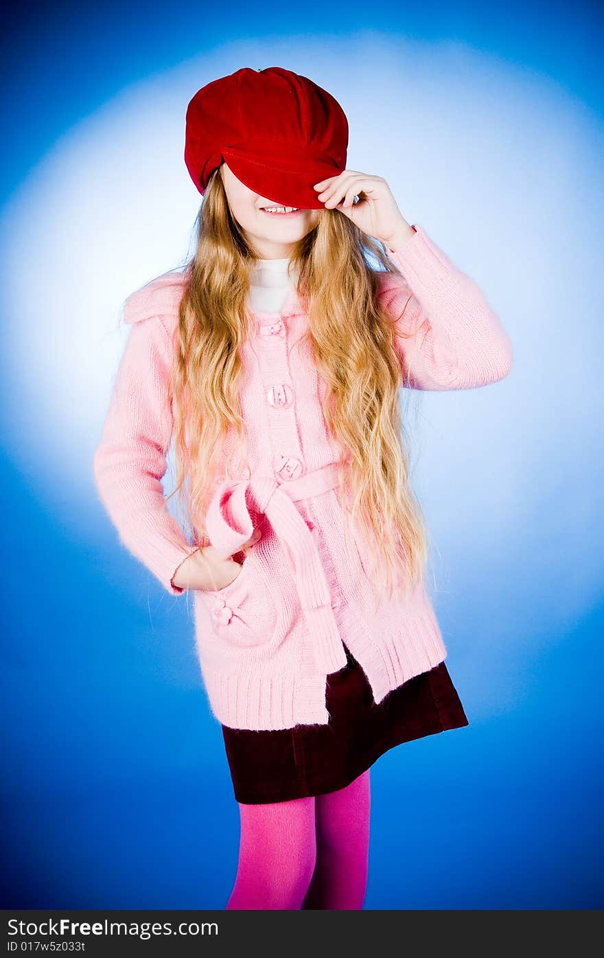 Funny little girl putting on red cap, studio shot