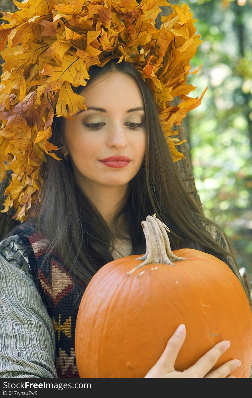 A beautiful young woman wearing a leaf wreath on her head and holding a pumpkin. A beautiful young woman wearing a leaf wreath on her head and holding a pumpkin