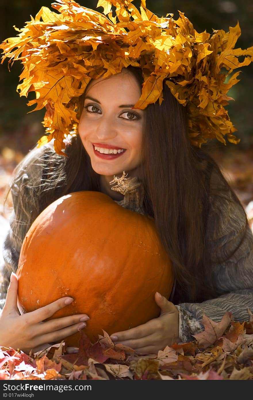 A young beautiful woman  wearing a leaf wreath on her head and holding a pumpkin. A young beautiful woman  wearing a leaf wreath on her head and holding a pumpkin