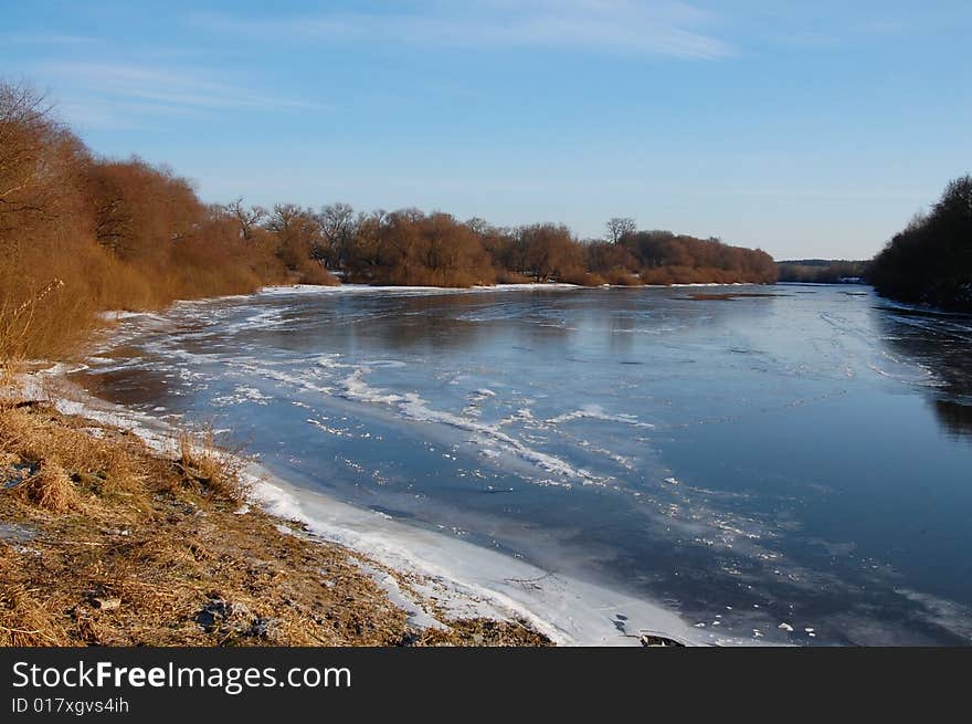 Blue sky and clouds reflection on icy cold river and brown bare bushes on the bank. Blue sky and clouds reflection on icy cold river and brown bare bushes on the bank