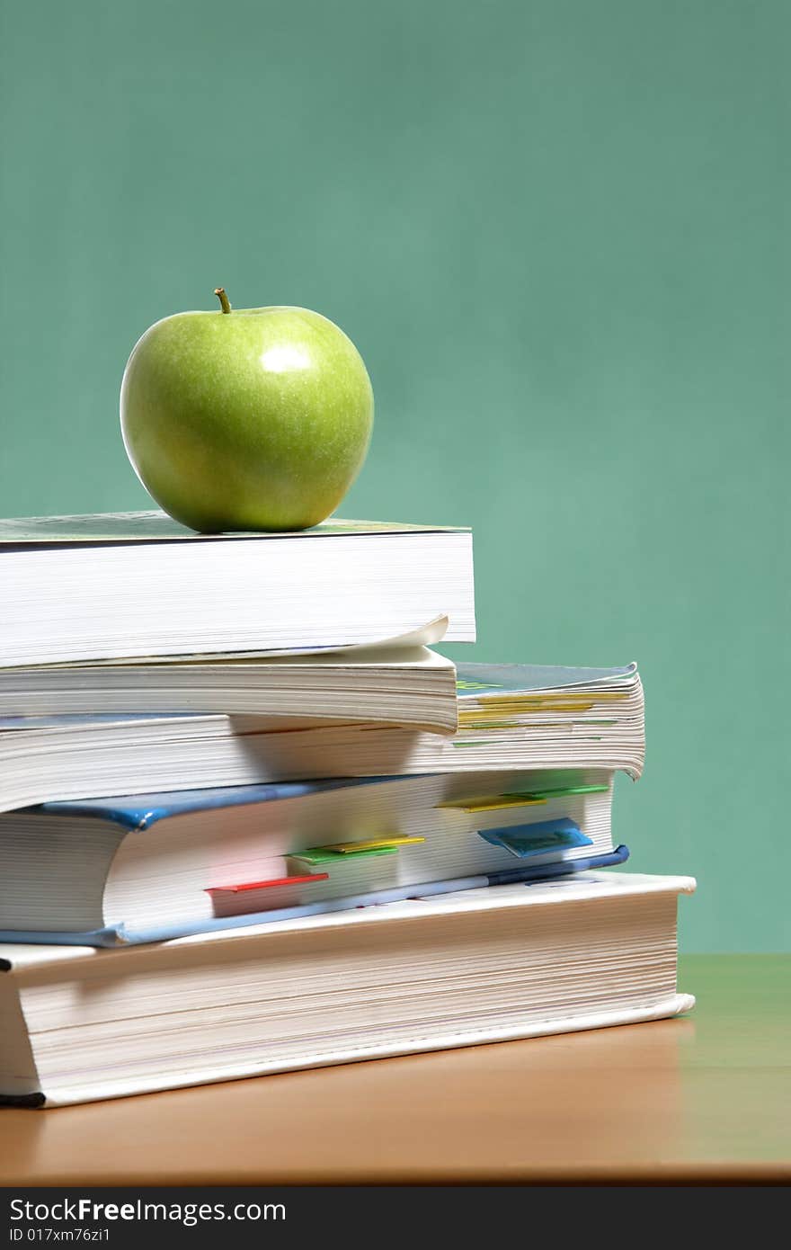 An apple on a stack of books on the teachers desk. An apple on a stack of books on the teachers desk