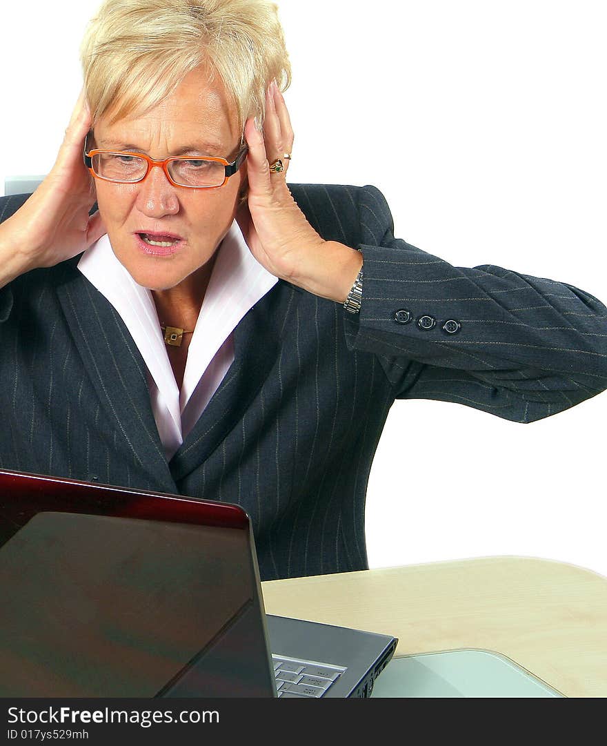 A businesswoman in her sixties in front of a laptop shocked with her hands on her head. Isolated over white. A businesswoman in her sixties in front of a laptop shocked with her hands on her head. Isolated over white.