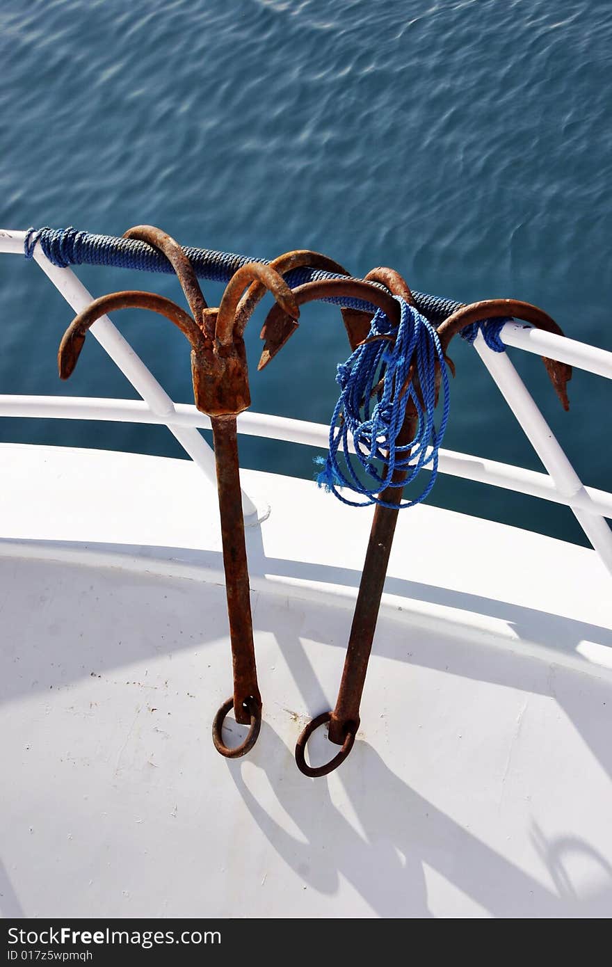 Two rusty anchors are hanging on a yacht handrail. Two rusty anchors are hanging on a yacht handrail