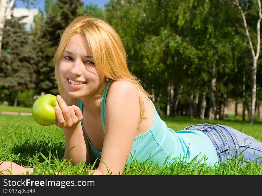 Pretty woman eating green apple on the summer glade