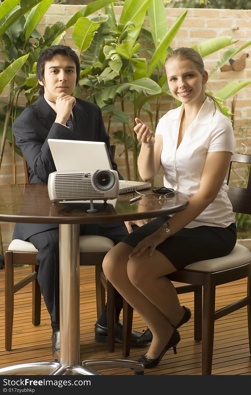 Man and woman with a projector and a laptop.. They are seated and she is smiling while he looks pensive. Vertically framed photo. Man and woman with a projector and a laptop.. They are seated and she is smiling while he looks pensive. Vertically framed photo.