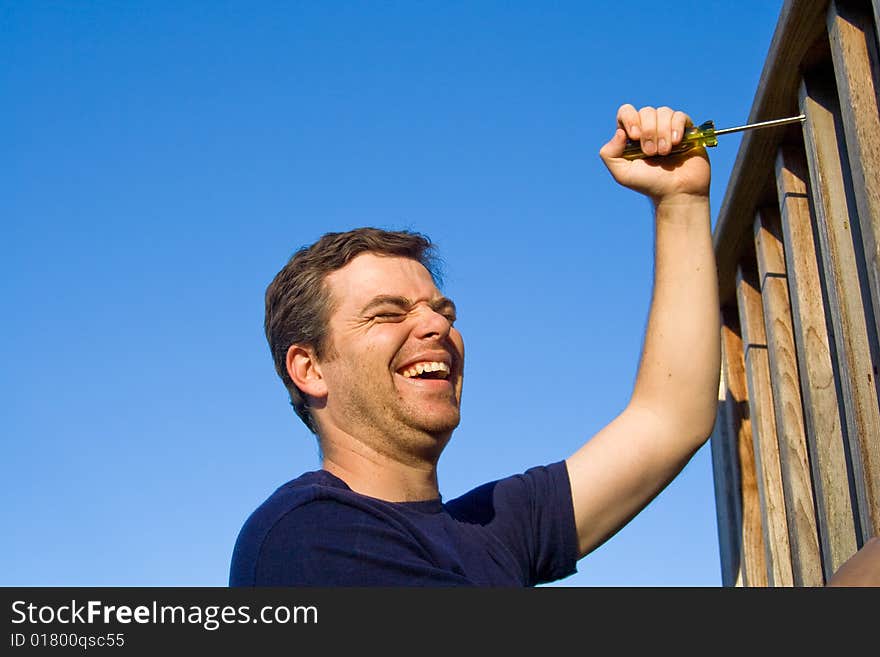 Laughing man using screwdriver to fix porch. Horizontally framed photo. Laughing man using screwdriver to fix porch. Horizontally framed photo.