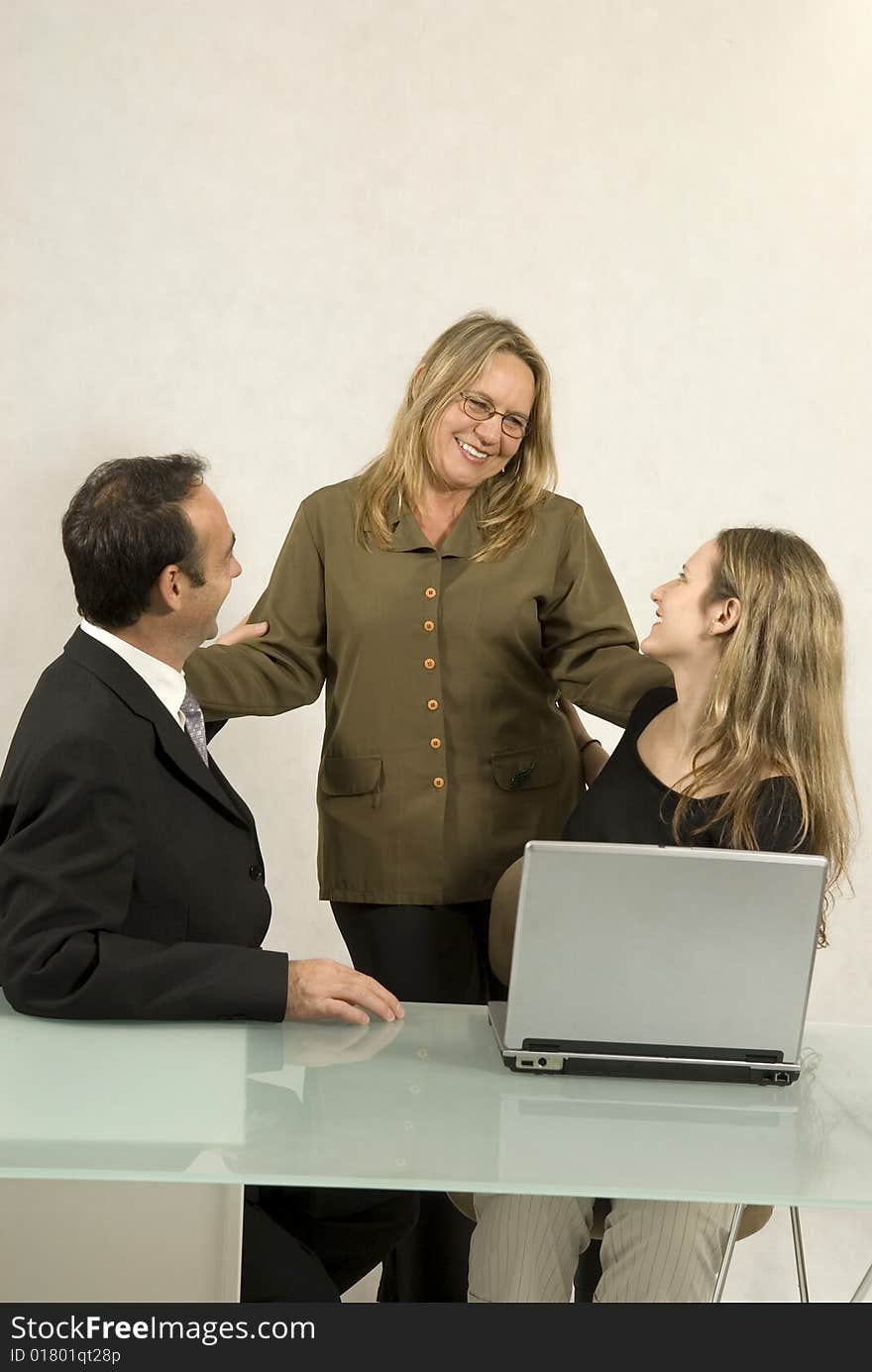 Three people are in a business meeting.  They are smiling and looking at each other.  There is a laptop on the table.  Vertically framed shot. Three people are in a business meeting.  They are smiling and looking at each other.  There is a laptop on the table.  Vertically framed shot.