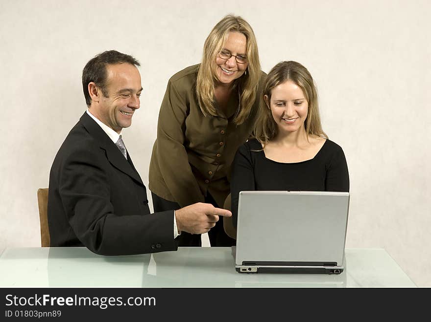 Three people are in a business meeting. They are smiling and looking at the screen of the laptop. Horizontally framed shot. Three people are in a business meeting. They are smiling and looking at the screen of the laptop. Horizontally framed shot.