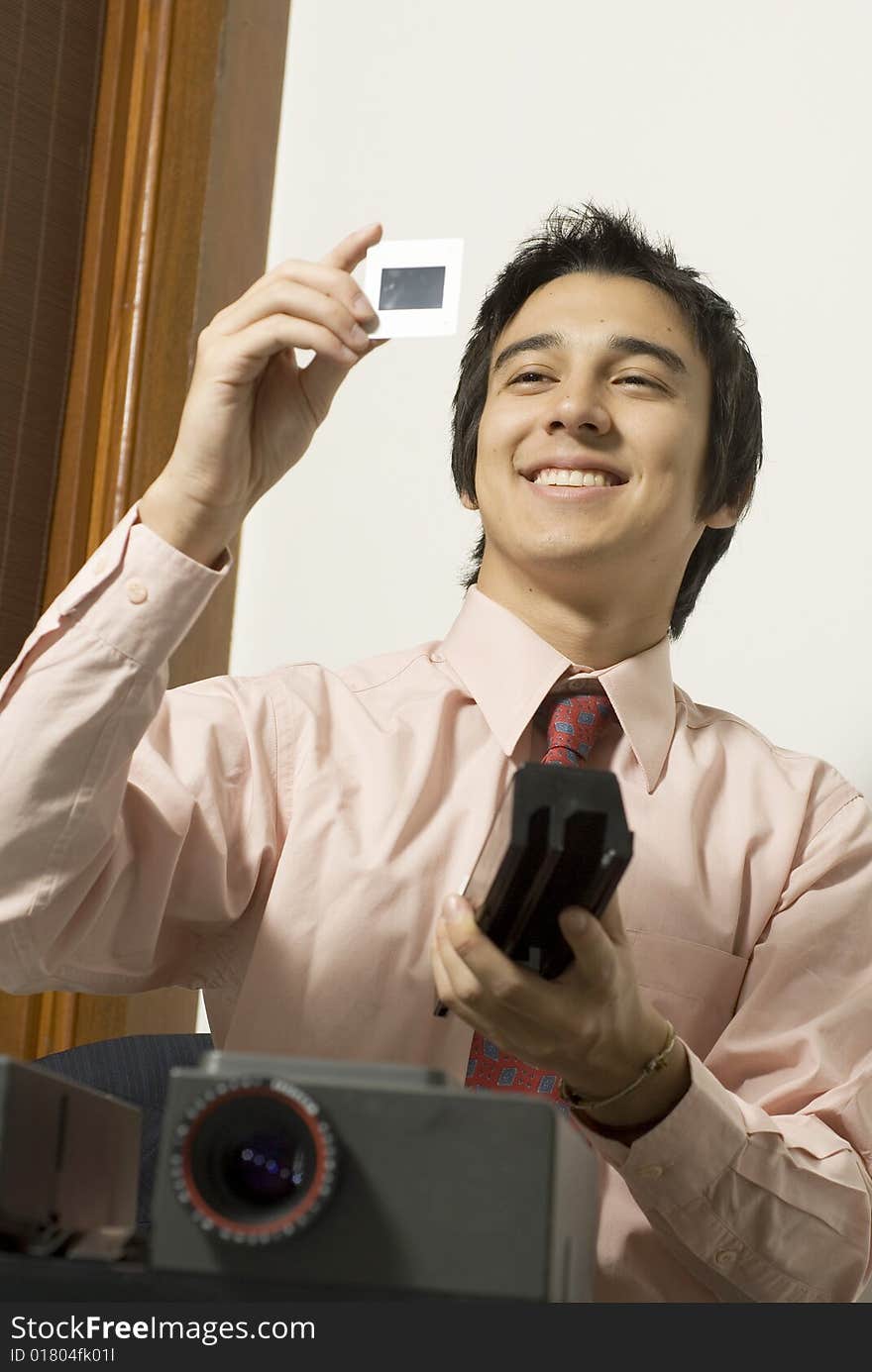 Man smiling as he looks at a slide next to a projector. Vertically framed photo. Man smiling as he looks at a slide next to a projector. Vertically framed photo.