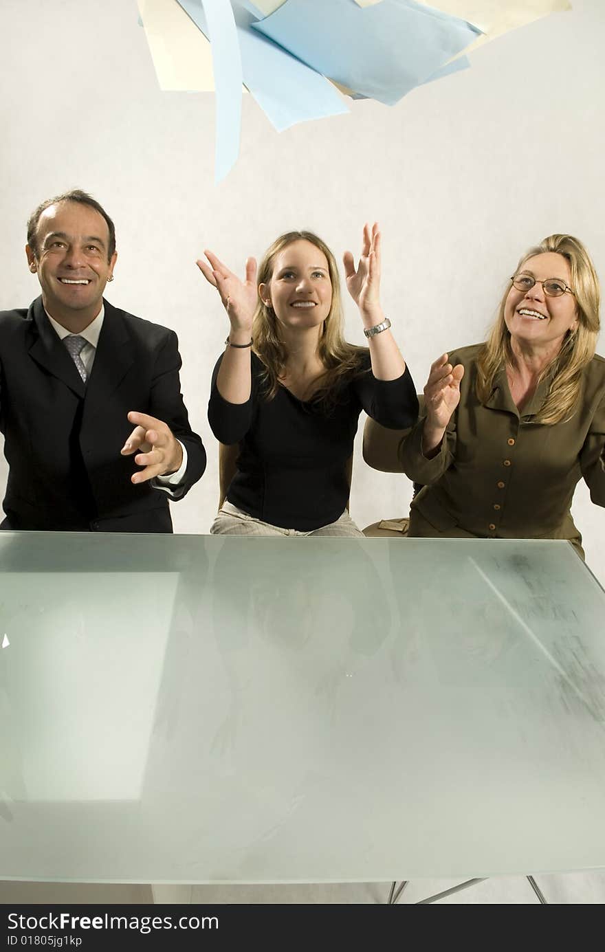 Three people are in an office in a meeting.  They are smiling and throwing papers in the air in success.  Vertically framed shot. Three people are in an office in a meeting.  They are smiling and throwing papers in the air in success.  Vertically framed shot.