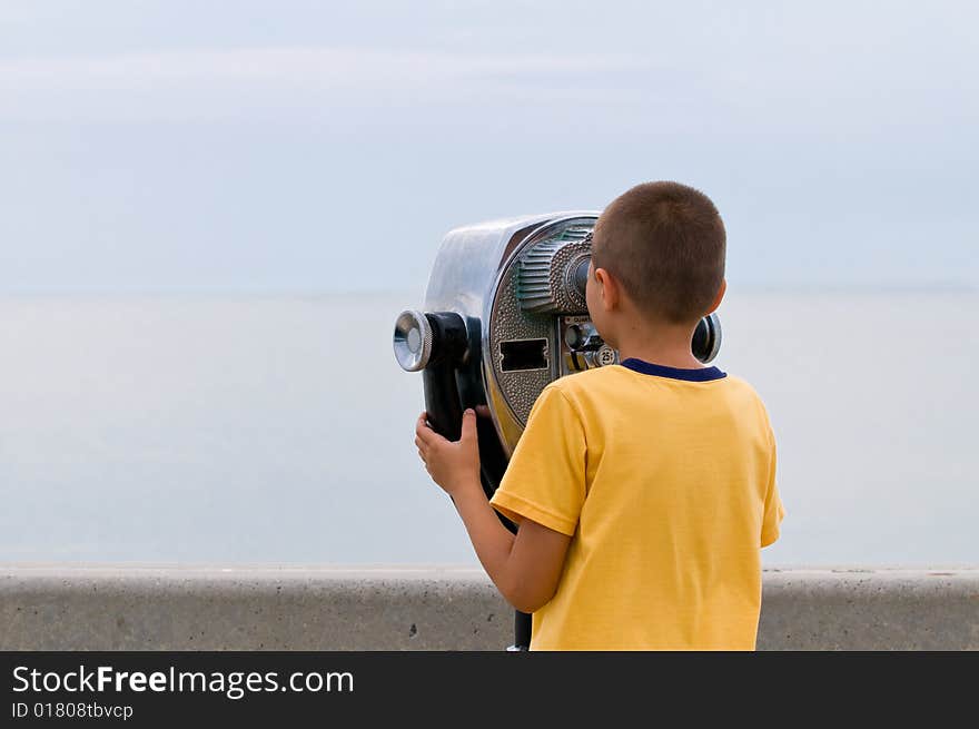 The boy looks through the coin operated binoculars on horizon. The boy looks through the coin operated binoculars on horizon