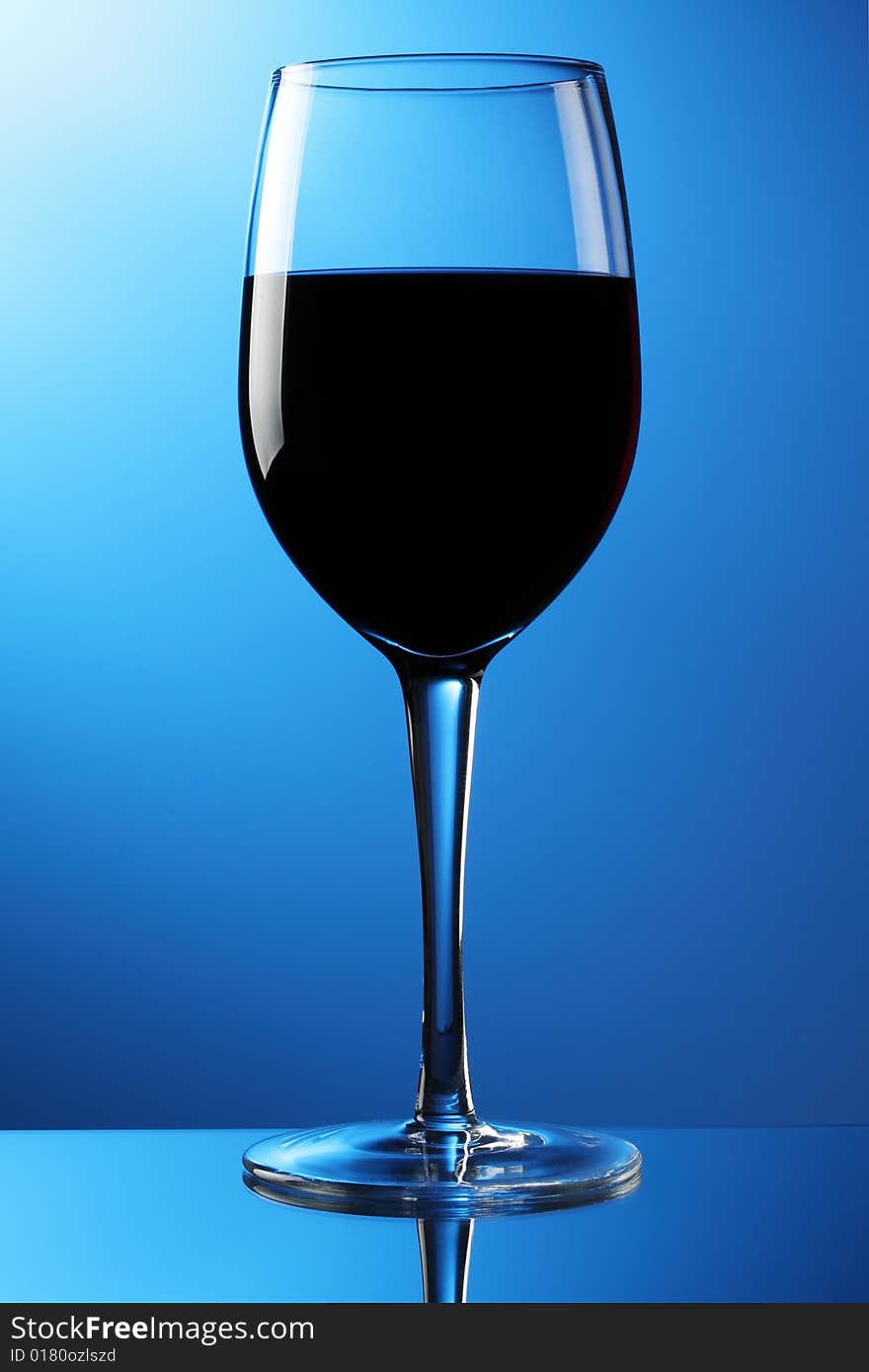 A glass of red wine on a reflective surface with blue graduated background. A glass of red wine on a reflective surface with blue graduated background.