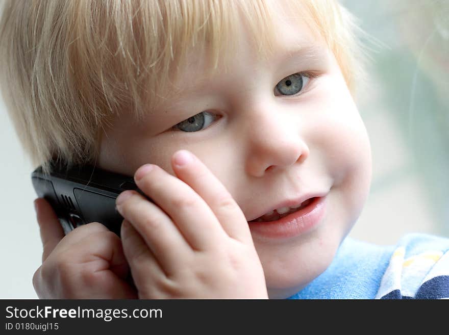 The child smiles and speaks on the telephone. The child smiles and speaks on the telephone