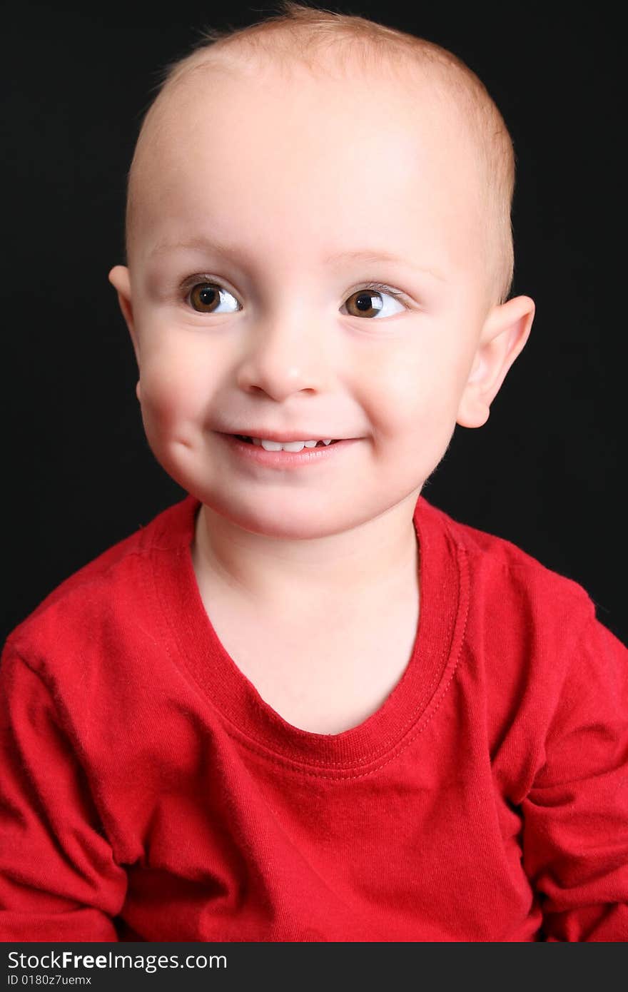 Blonde toddler against a black background with a big smile