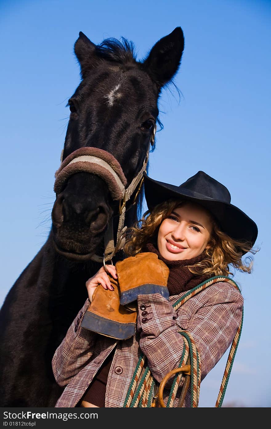 Lovely blond woman in a hat standing by horse in a field