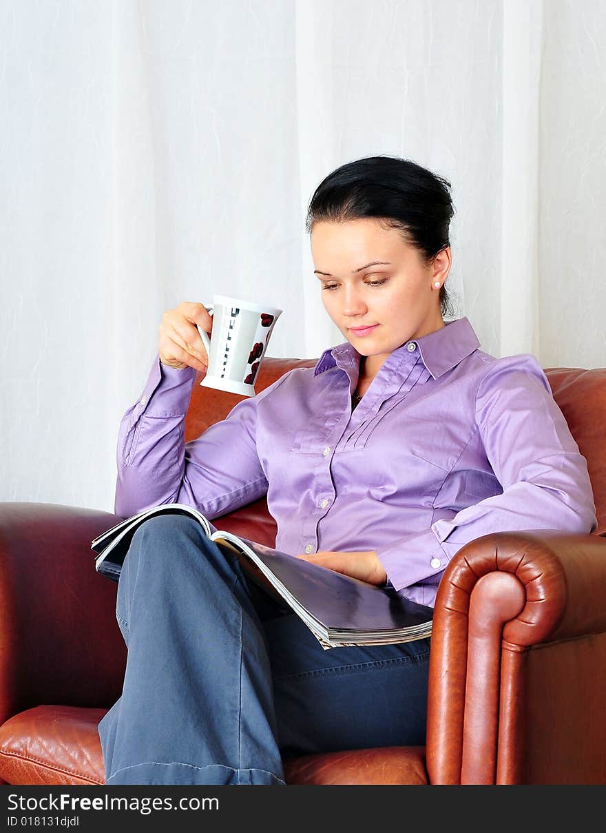 Beautiful young girl drinking coffee and reading magazine